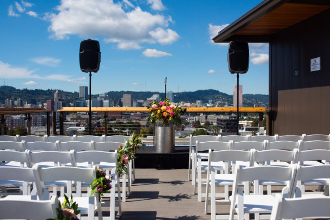 The roof deck set up for a wedding, seating on either side, pulpit with flowers in background.